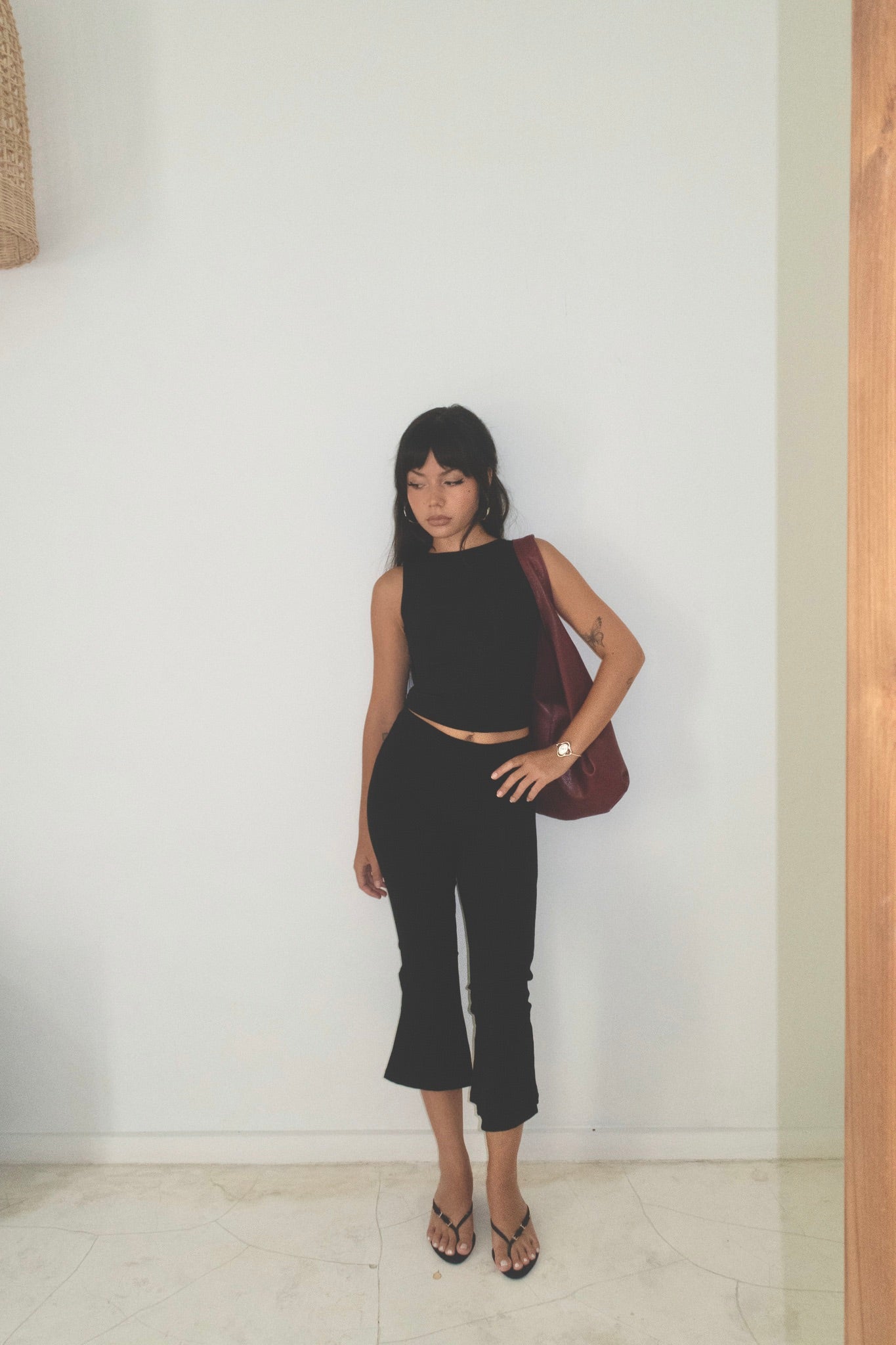Woman in black outfit holding a red bag against a white wall