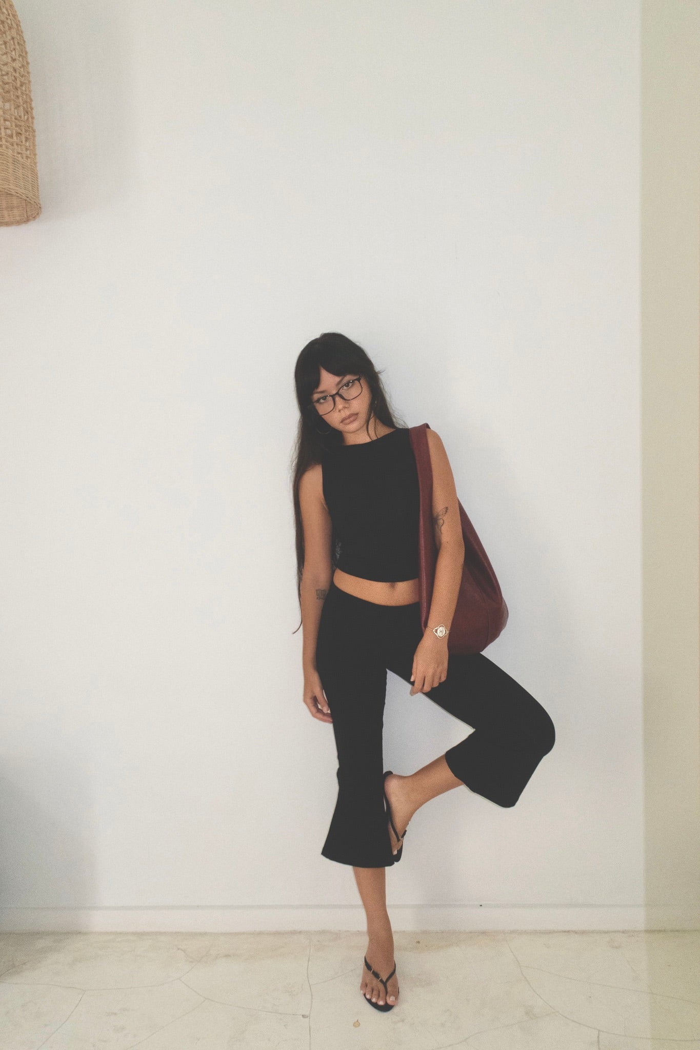 Woman in black outfit with a red bag against a white wall