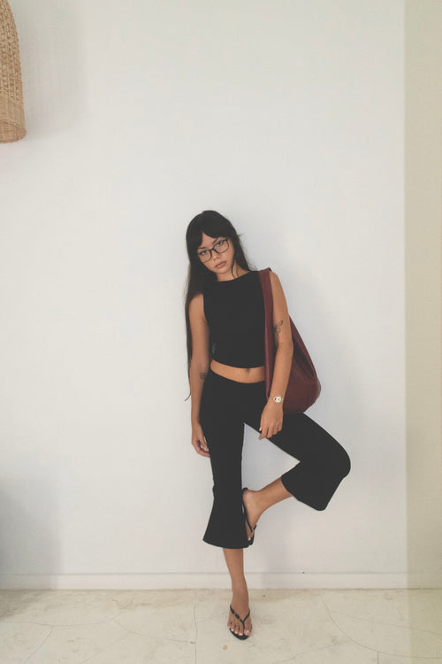 Woman in black outfit with a red bag against a white wall